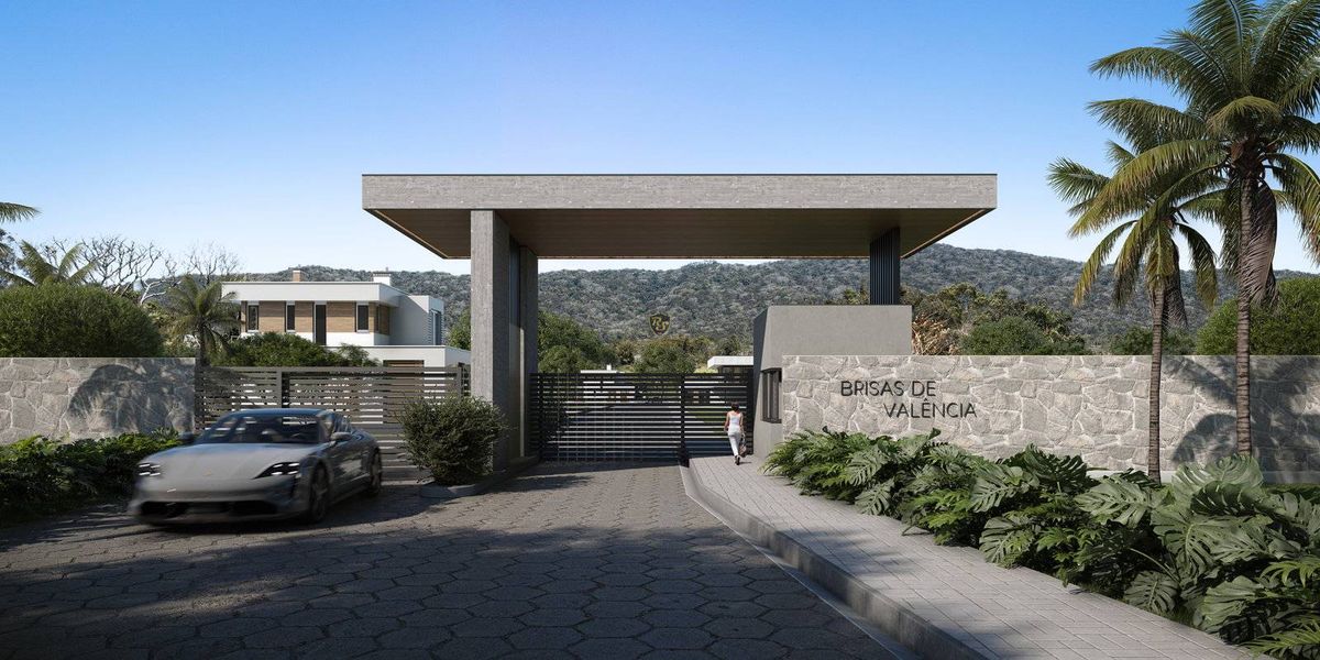 Entrada da residência com muro, portão de ferro e jardim decorativo.