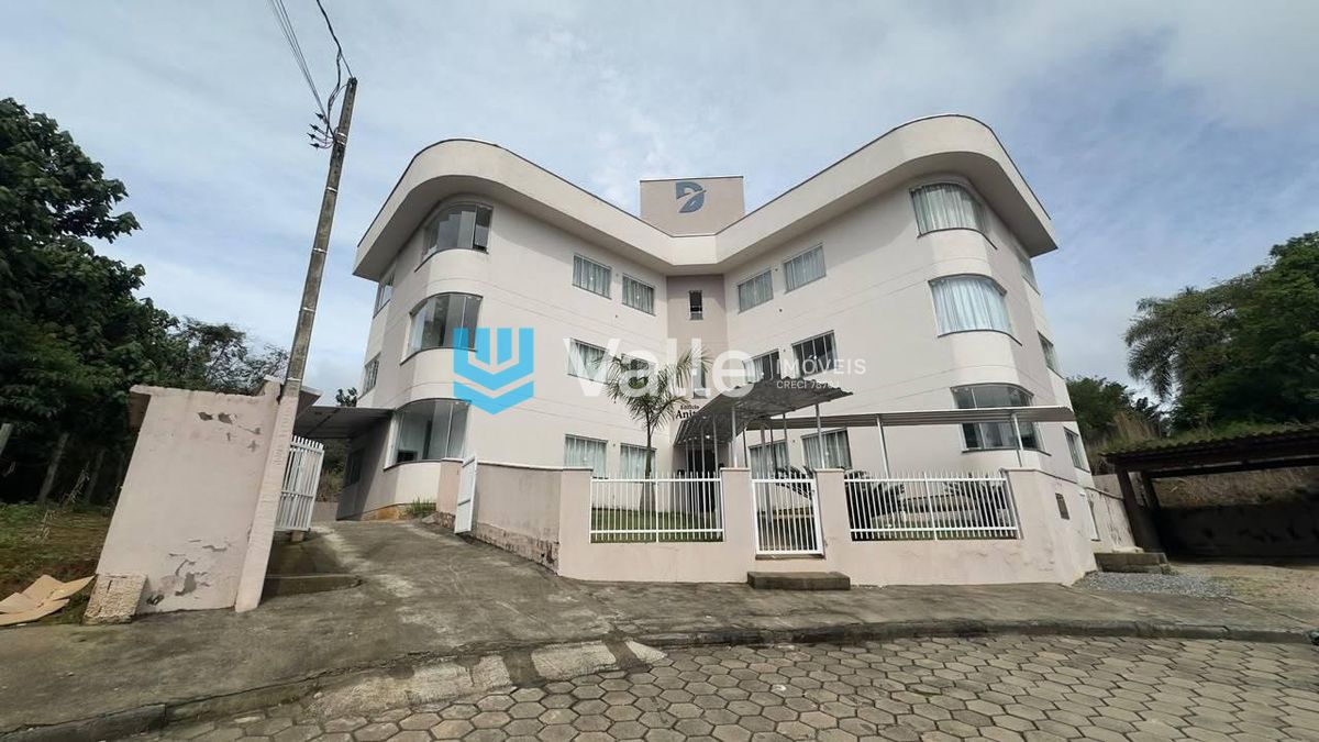 Edifício branco de arquitetura moderna com janelas curvilíneas, cerca e vegetação.