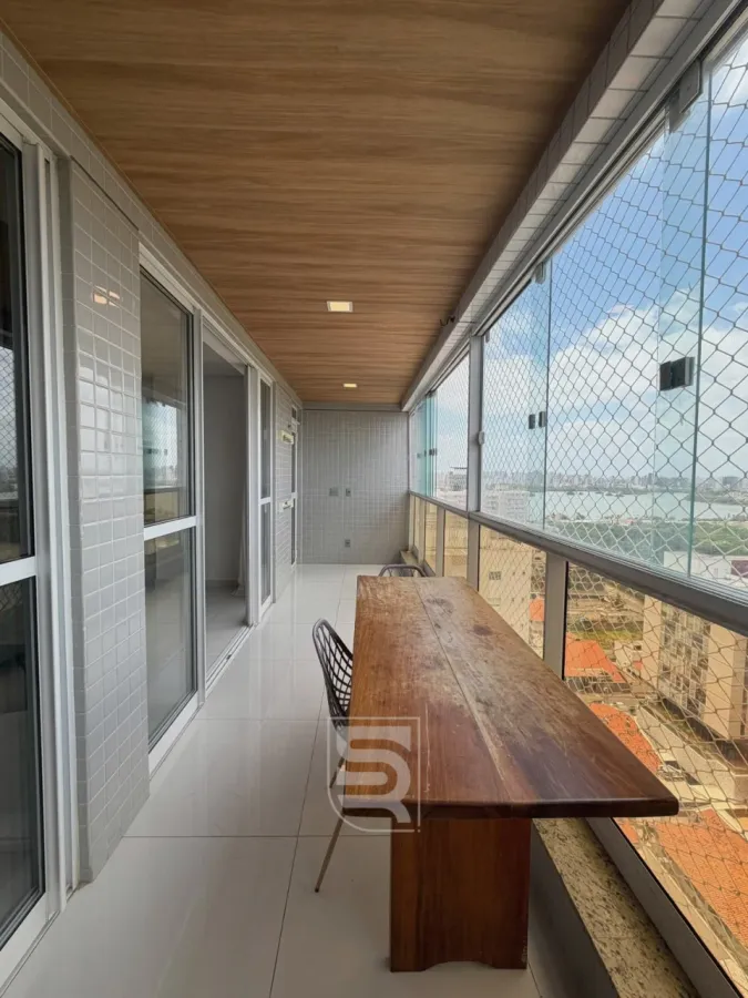 Varanda com mesa de madeira, vista para a cidade e grade de proteção.