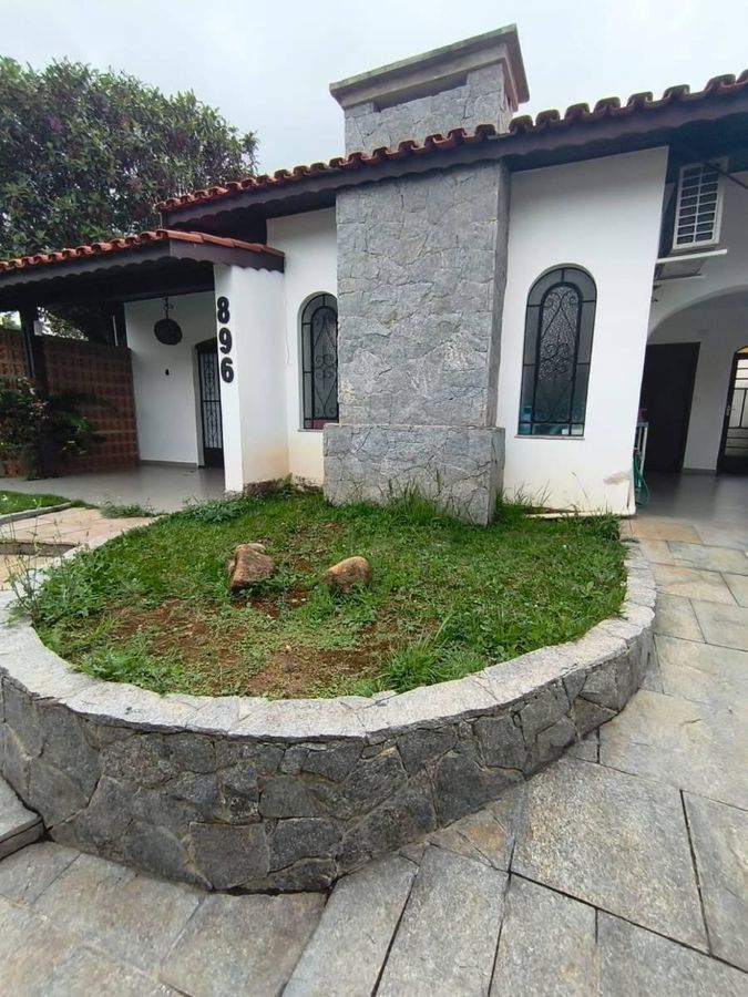 Fachada de casa com paredes brancas, janelas de vidro e cobertura de telhas vermelhas.