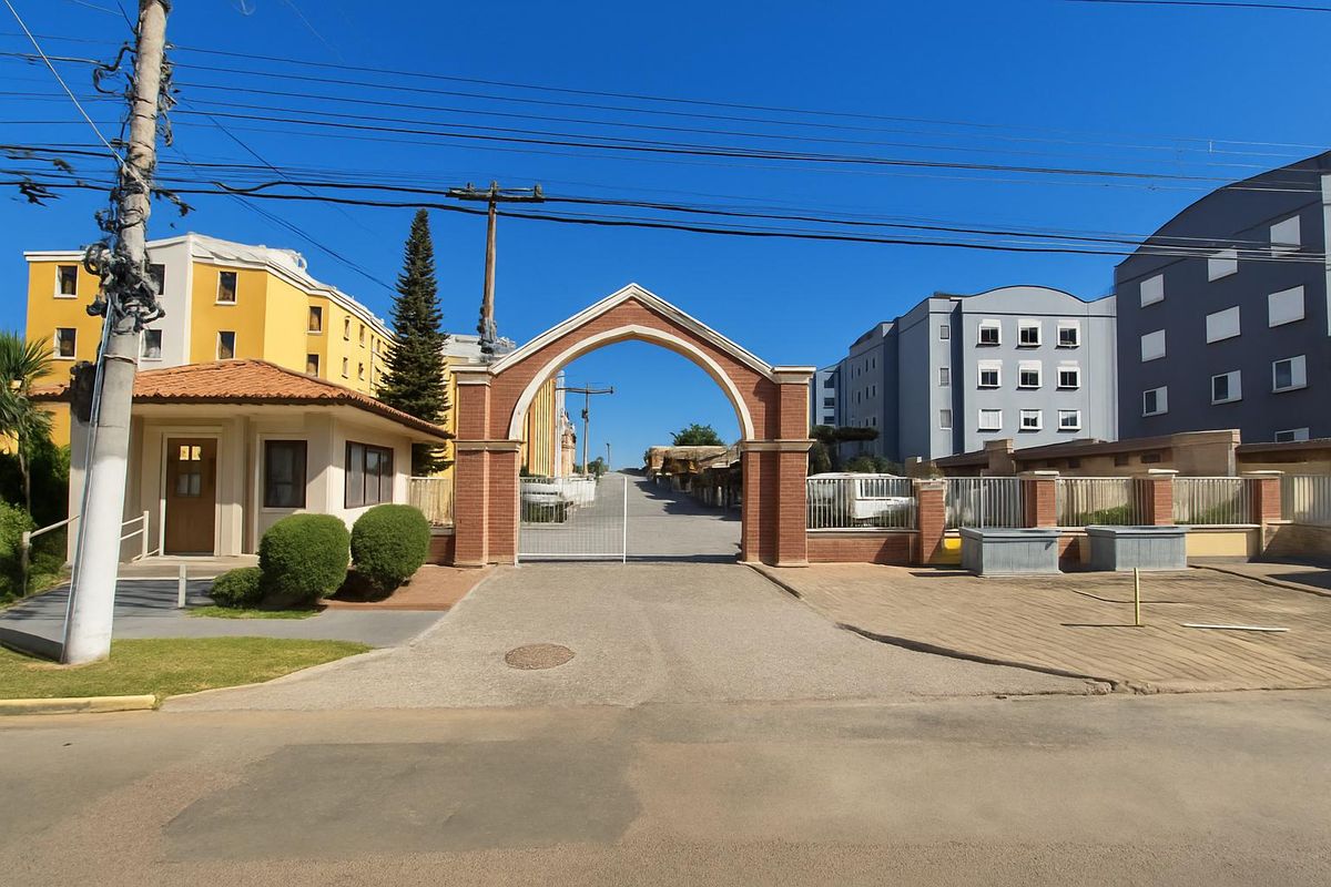 Entrada de condomínio com portal de tijolos, pavimentação e prédios ao fundo