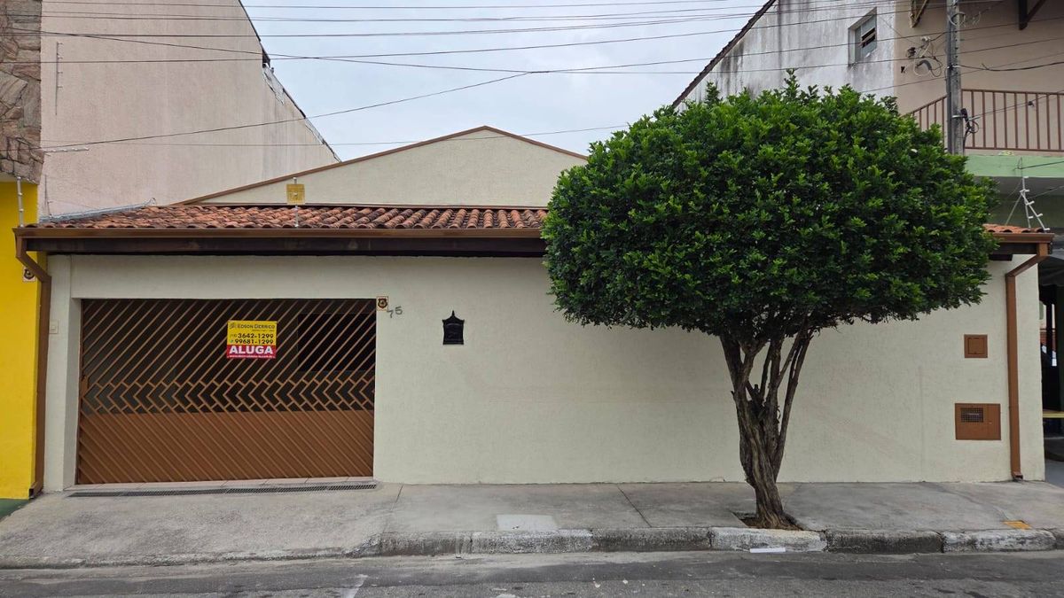 Fachada de casa com muro, porta de metal e árvore na calçada