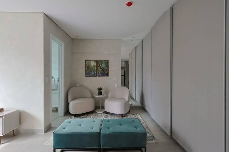 Sala com paredes claras, dois sofás curvos, armários brancos e quadro
