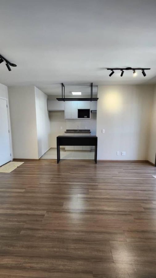Sala com cozinha integrada, piso de madeira e iluminação fixa no teto