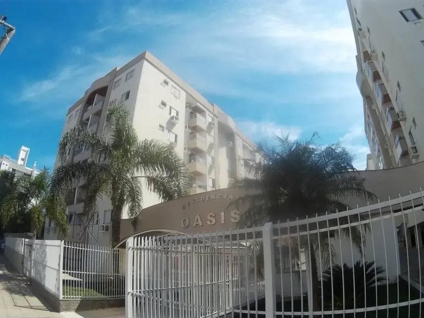 Prédio residencial alto com fachada branca, cercado por árvores e alambrado.