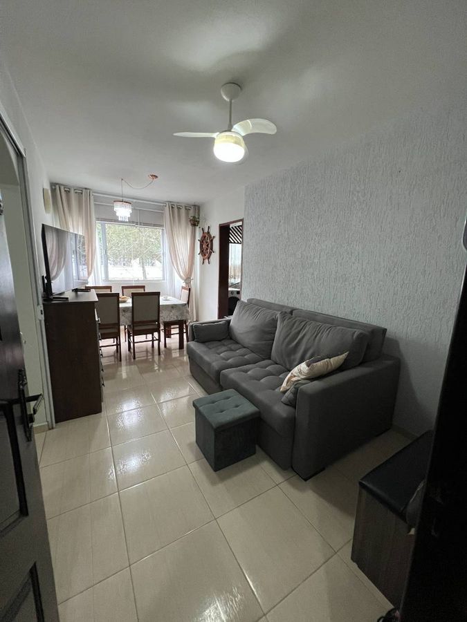 Sala com sofá cinza, TV, mesa de jantar e cortinas brancas.