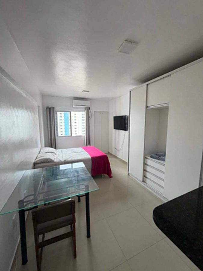 Quarto com cama, janela, televisão e armário branco, piso de porcelanato.