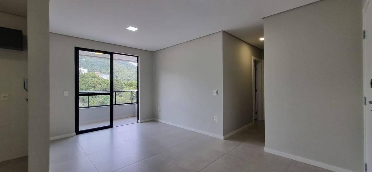 Sala com parede branca, piso claro, janela com vista para natureza