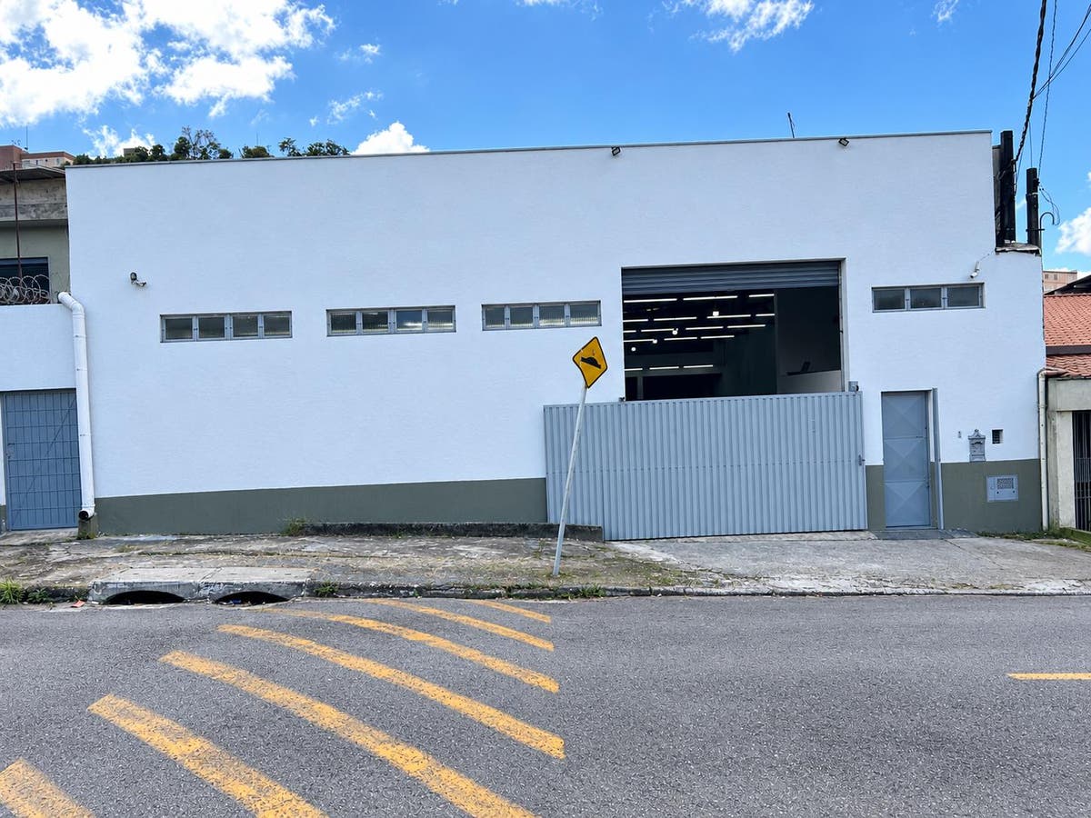 Fachada de prédio comercial branco com portão de metal cinza, porte fechado