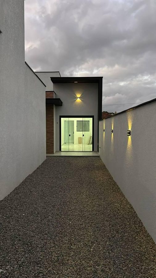 Entrada de residência moderna com parede branca, iluminação externa, piso de pedrisco