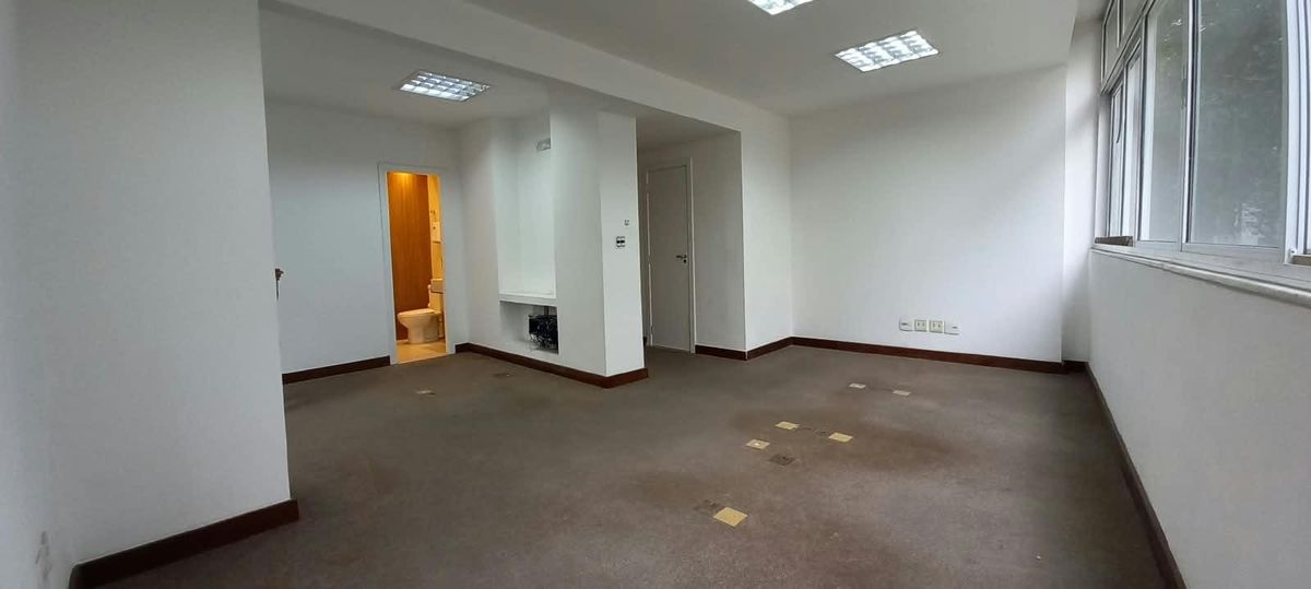 Sala com paredes brancas, piso de carpete e janelas grandes.