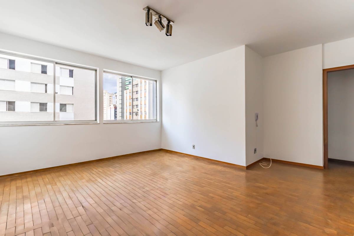 Sala com janelas amplas, piso de madeira clara e paredes brancas.