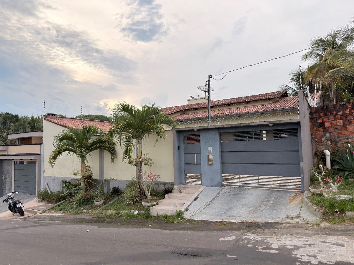 Casa com muro, portão de metal, jardim com plantas tropicais, calçada de concreto