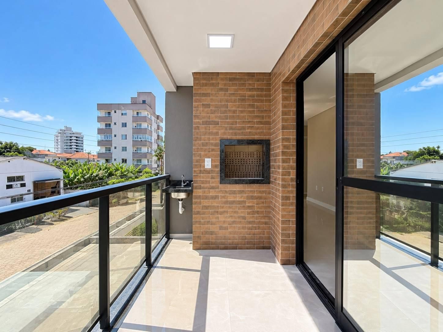 Varanda com parede de tijolos, churrasqueira, piso claro, vista urbana