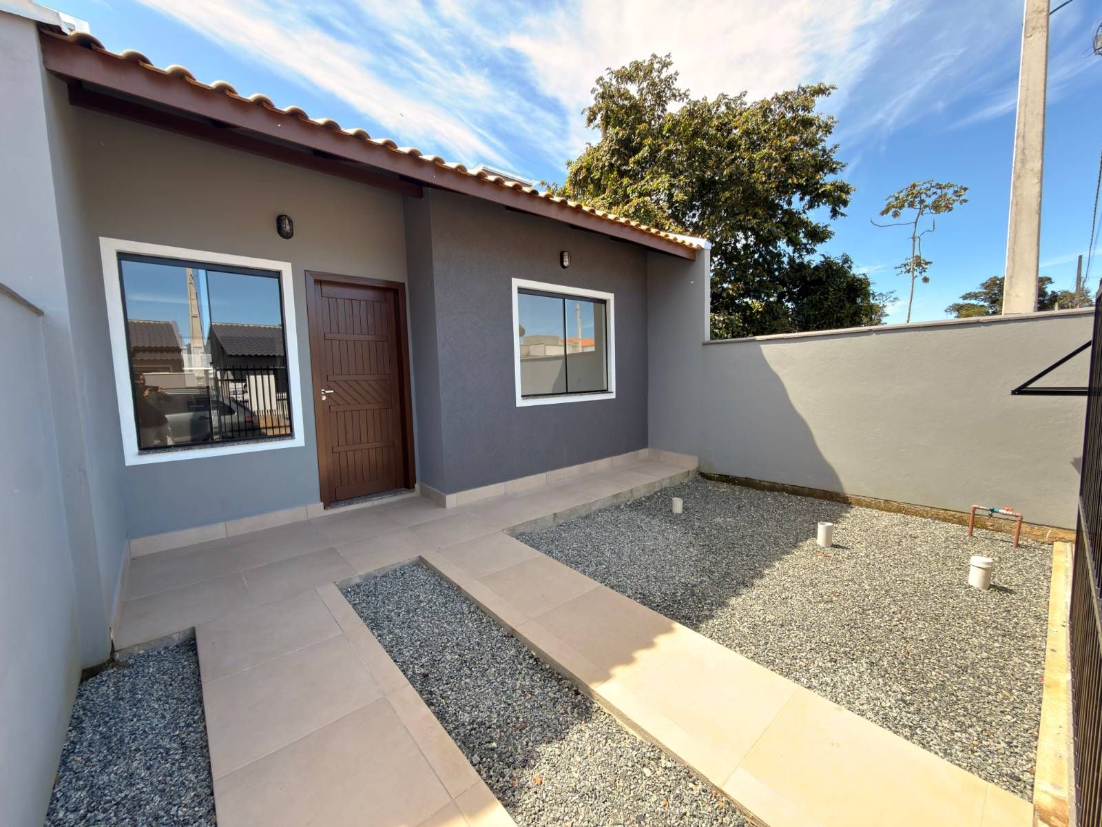 Varanda com piso de cerâmica, muro e árvores ao fundo