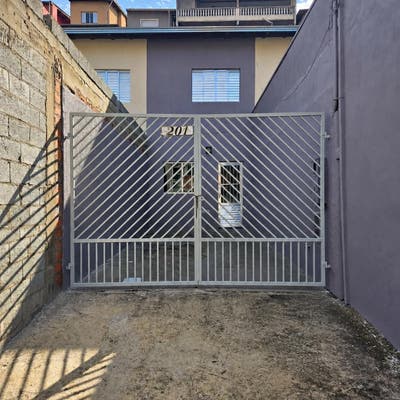 Fachada de residência com muro de blocos e portão de metal branco.