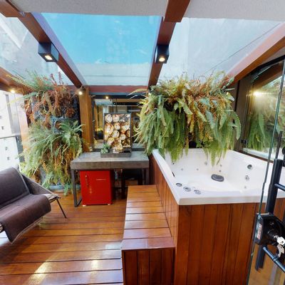 Varanda com jacuzzi, plantas verdes e teto de vidro, ambiente aconchegante.