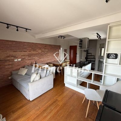 Sala com parede de tijolos e piso de madeira, ambiente integrado.