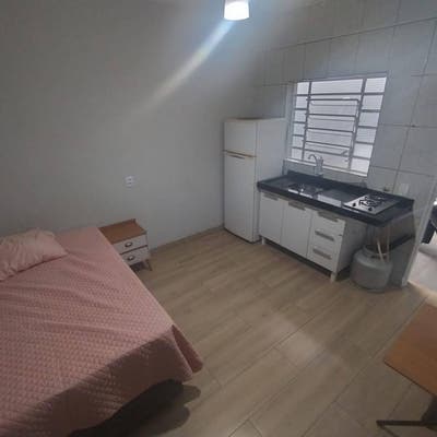 Quarto com cama, cômodo de parede lisa, cozinha integrada, janela de grades.