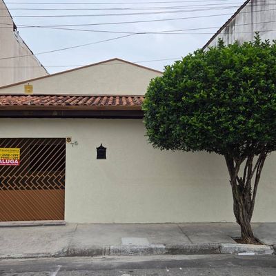 Fachada de casa com muro, porta de metal e árvore na calçada
