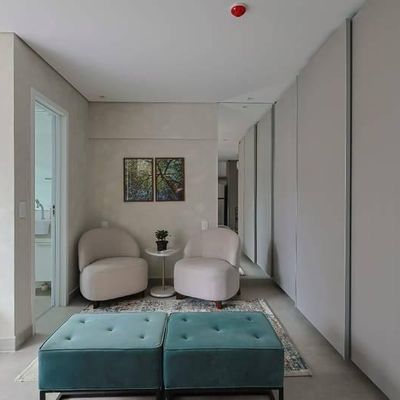 Sala com paredes claras, dois sofás curvos, armários brancos e quadro