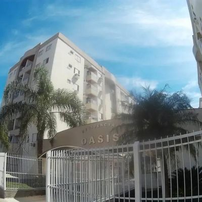 Prédio residencial alto com fachada branca, cercado por árvores e alambrado.