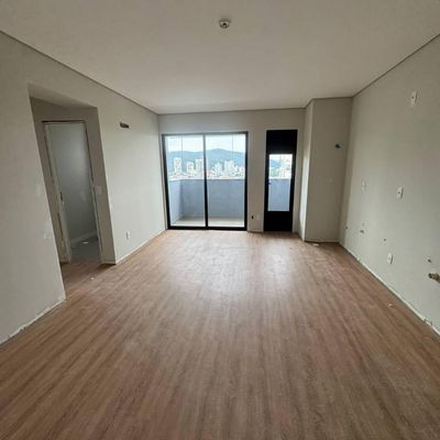 Sala vazia com piso de madeira, janelas de vidro e varanda.