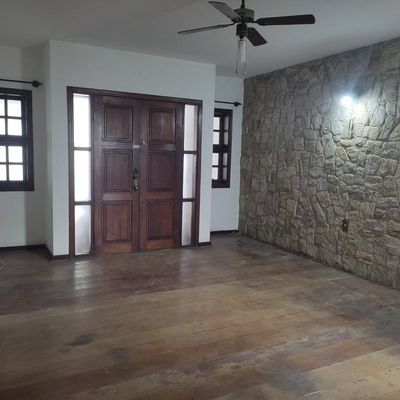 Sala com fachada de pedra, piso de madeira, janelas com persianas pretas