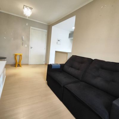 Sala com sofá preto, paredes claras, piso de madeira, iluminação artificial