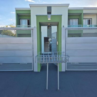 Prédio residencial com fachada branca e detalhes verdes, portão de metal