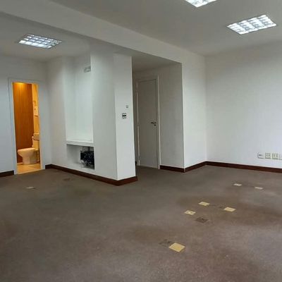 Sala com paredes brancas, piso de carpete e janelas grandes.