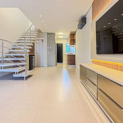 Sala com parede clara, piso de cerâmica, iluminação embutida, televisão grande