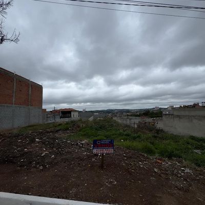 Lote vazio com grama, cercado por paredes de alvenaria e céu nublado
