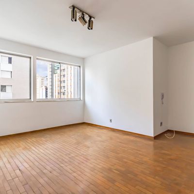 Sala com janelas amplas, piso de madeira clara e paredes brancas.