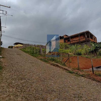Estrada de pedra com casa em construção e vegetação ao redor.