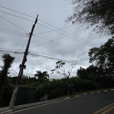 Céu nublado, postes de energia, árvores ao lado de rua asfaltada.
